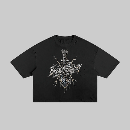 A black short-sleeve crop top t-shirt featuring a detailed graphic print on the front. The graphic depicts a crowned skeleton figure with lightning bolts and the stylized text 'BREAD OVER GLORY' in white and silver.