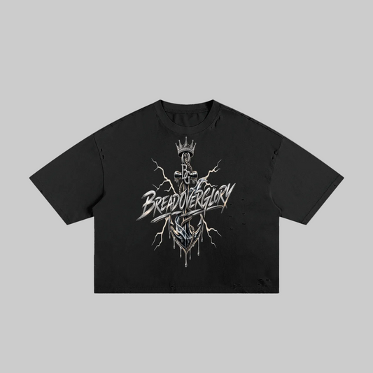 A black short-sleeve crop top t-shirt featuring a detailed graphic print on the front. The graphic depicts a crowned skeleton figure with lightning bolts and the stylized text 'BREAD OVER GLORY' in white and silver.